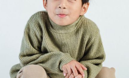 Kids' Fashion Trends - Full body of adorable Asian child wearing trendy casual wear sitting on hunkers against white background